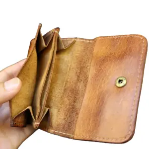 Geöffnetes braunes Ledergeldbeutelchen mit Druckknopf und Münzfach in der Hand gehalten