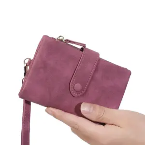 Beerenfarbenes Damen-Portemonnaie aus Veloursleder-Optik mit Lasche und Handschlaufe in der Hand