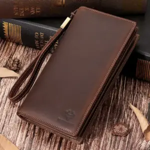 Dunkelbraune lange Lederbörse mit Handschlaufe auf Holztisch neben Büchern